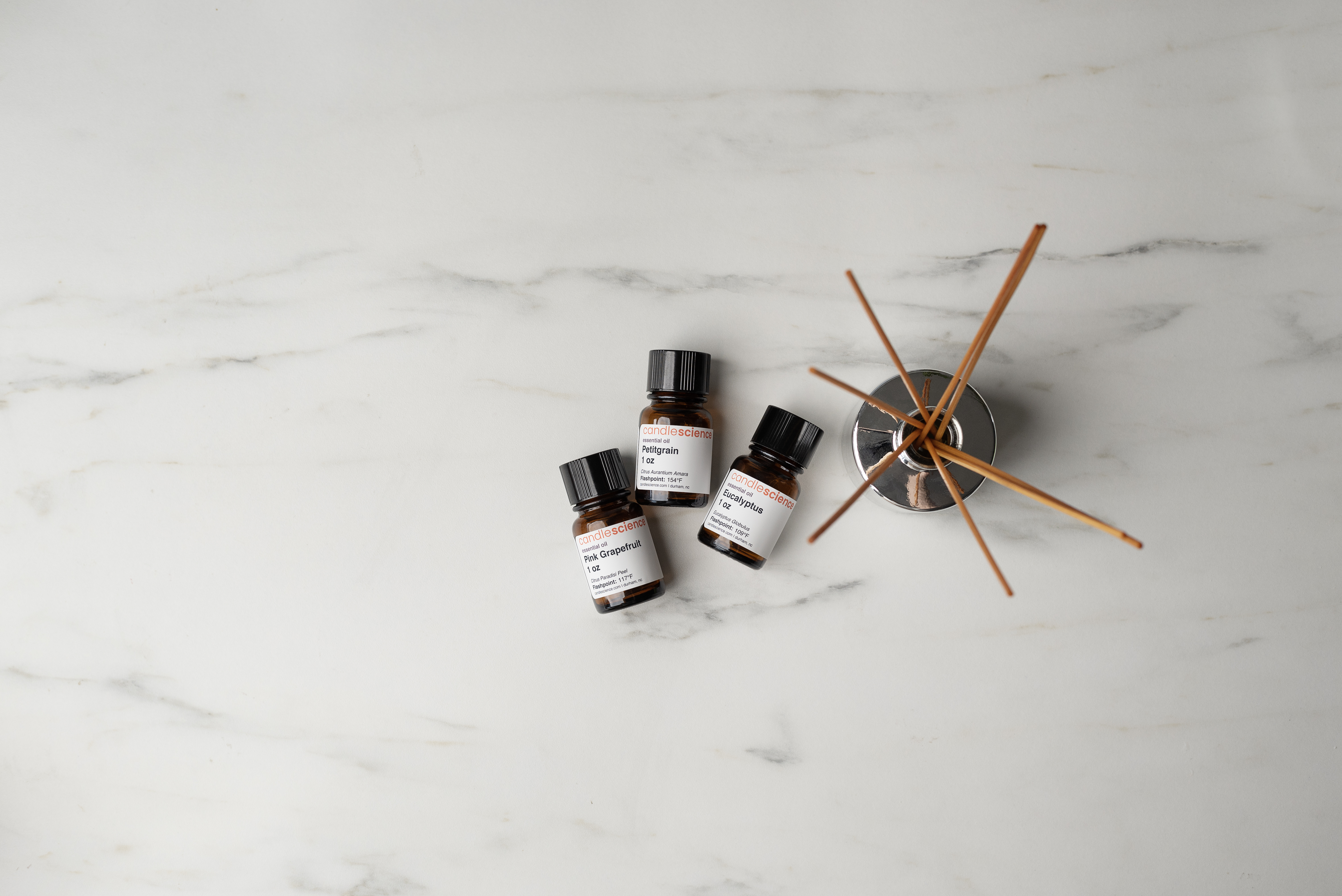 Essential oil bottles next to reed diffuser bottle with rattan reeds.