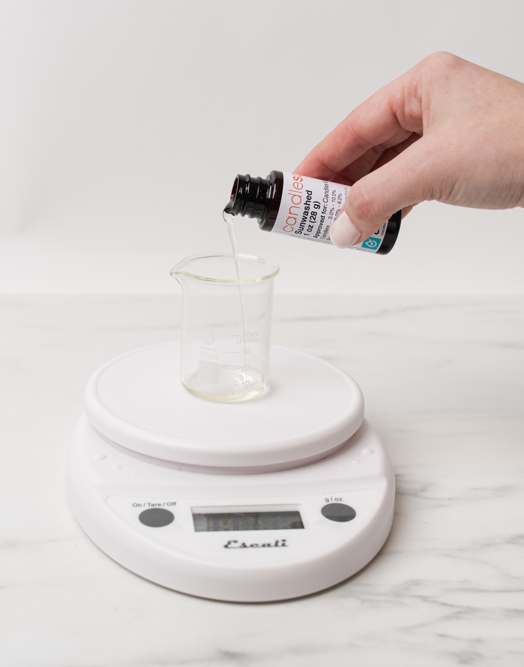 Pouring fragrance oil into glass beaker on scale.