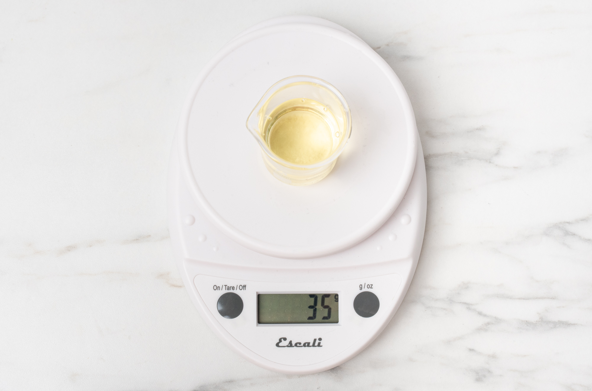 Glass beaker of fragrance oil on scale.