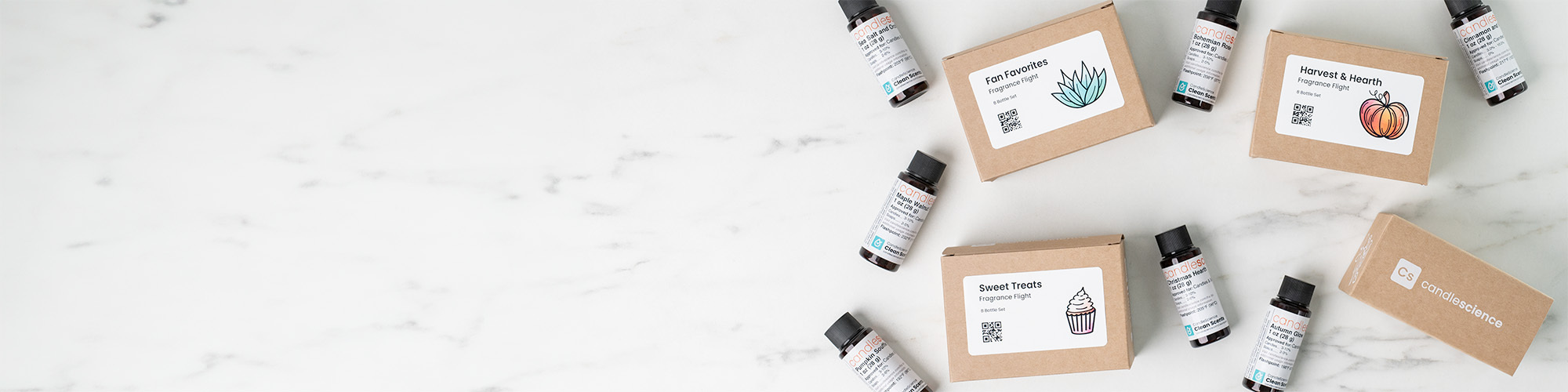 Looking down on a marble countertop with several small, kraft fragrance flight boxes with colorful labels. Several 1 oz fragrance bottles are mixed in.