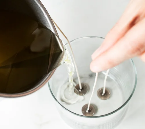 hot wax being poured into a clear container with three candle wicks
